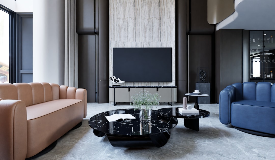 Modern luxury living room with smart home technology featuring contemporary grey and beige furniture, wall-mounted flat screen TV on textured white panel, floor-to-ceiling windows, and sophisticated interior design